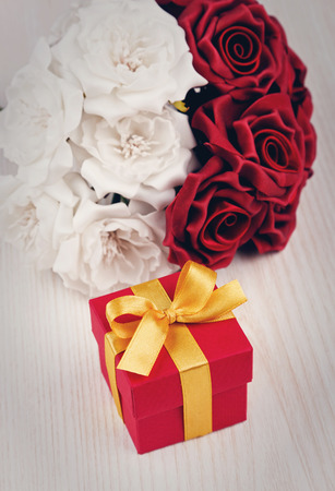 red and white roses and red gift box with yellow ribbon on wooden surfaceの写真素材