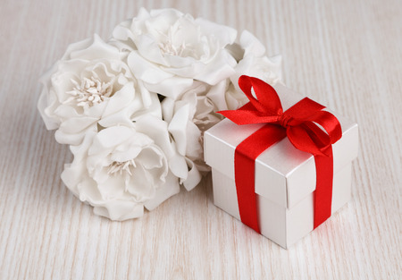 white flowers and  gift box with red ribbon on wooden surfaceの写真素材