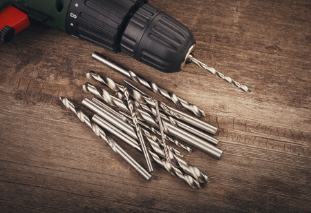 Drill and set of drill bits with screws on wooden backgroundの写真素材