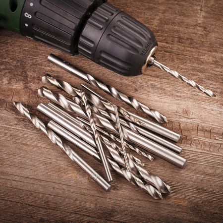 Drill and set of drill bits with screws on wooden backgroundの写真素材