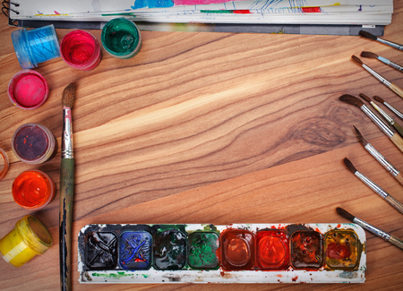 Colorful paints and brushes arranged as a frame on wooden tableの写真素材