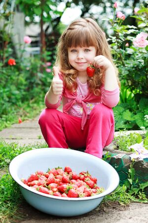Little girl eating ripe strawberries, bowl in front of her,  and say OKの写真素材