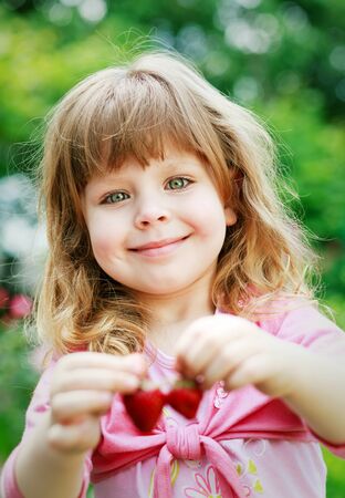 Little girl hold and eating  ripe strawberries, focus on the faceの写真素材