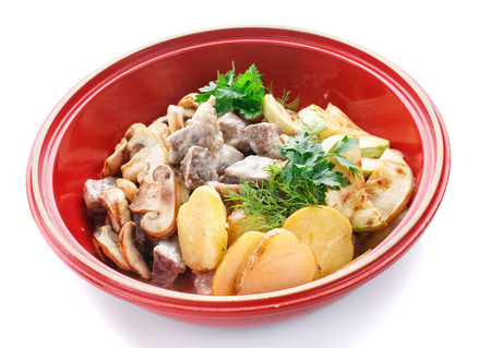 meat with mushrooms and vegetables in a pot on a white backgroundの写真素材
