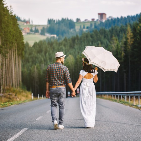 happy loving couple walking along the road in the forest. A girl in a white dress and with umbrellaの写真素材