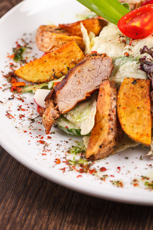 restaurant meals, delicious food, fried foods - salad with fresh vegetables grilled veal and baked potatoes on the plate on a wooden table.の写真素材