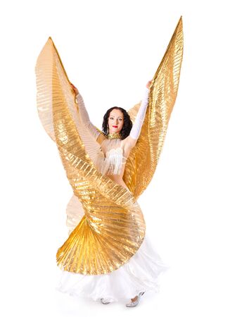 Beautiful young girl in a white suit oriental dance in motion with big golden wings isolated on white backgroundの写真素材