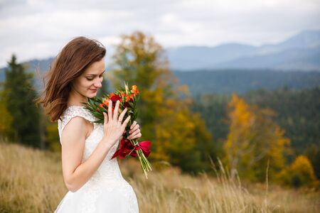 Romantic beautiful bride in white dress posing on the background mountainsの写真素材