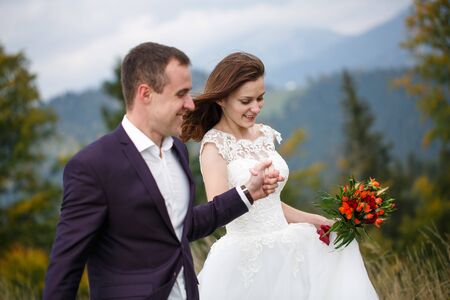 Love, Adventure, and Nature Concept. Loving couple walking in the lawn on the background of majestic mountains. Newlyweds celebrate the wedding.の写真素材