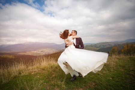 Loving couple are newlyweds in the mountains. Stylish bride with a bouquet kisses the groom. love, fidelity and shadowing concept. Mountain Walk and Hiking.の写真素材