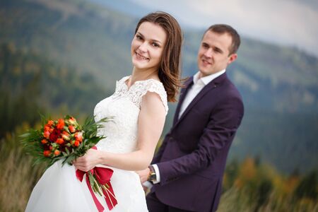 Love, Adventure, and Nature Concept. Loving couple walking in the lawn on the background of majestic mountains. Newlyweds celebrate the wedding.の写真素材