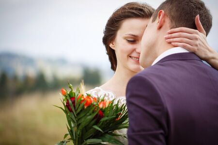 Portrait of a Lovely Couple Newlyweds in the Mountains. A stylish bride with a bouquet kisses the groom. A beautiful and aesthetic photo illustrates love.の写真素材