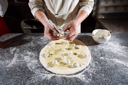 Pitseriyne dough in the hands of the chef. decomposition of the filling on the dough. Dough on the table. Cooking pizza in the pizzeria.の写真素材
