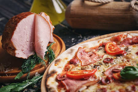Pizza with sausages, ham, mushrooms and tomatoes. Poster for Restaurants or pizzerias. Pizza on a black backgroundの写真素材