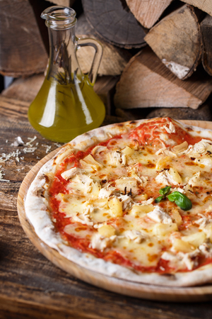 Pizza with chicken and pineapple on the background of firewood. Concept promotional flyer. Pizza on a wooden backgroundの写真素材