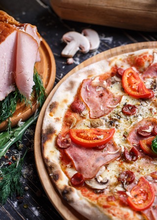 Pizza with sausages, ham, mushrooms and tomatoes. Background ready for your design. Pizza on a black backgroundの写真素材