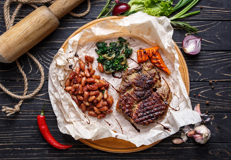 Concept promotional flyer. Meat and pepper from the grill placed along with beans and salad. On a black wooden background. . Flay lay. Top viewの写真素材