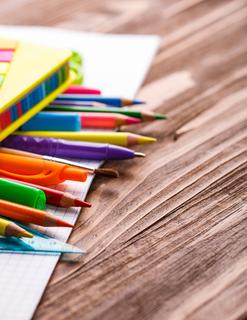 Bright pens and pencils scattered on a notebook. School objects for students. On a wooden background. flat lay. selective focusの写真素材