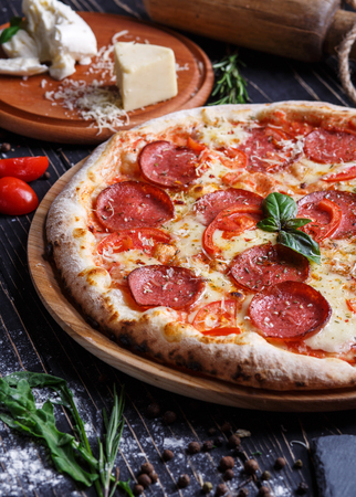 Aromatic pizza with sausage and tomatoes is decorated with basil. Concept promotional flyer. Pizza on a black backgroundの写真素材