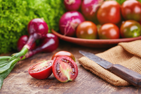 On a wooden table onion, tomatoes, greens and knifes.の写真素材