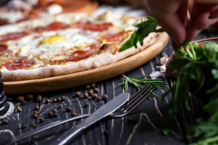 Cutlery near pizza and greenery. A fragment of pizza. Poster for Restaurants or pizzerias. Pizza on a black backgroundの写真素材