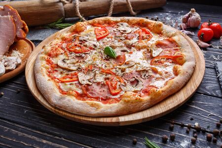 Pizza with vegetables, mushrooms, ham and mozzarella. Poster for Restaurants or pizzerias. Pizza on a black backgroundの写真素材