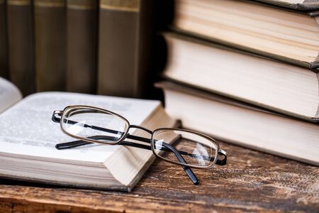 The glasses lie on the open book in the library. The glasses lie on open book on the background of books and the old watch. 1 September concept postcard, teachers dayの写真素材