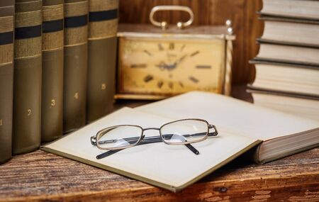 Open books ready for reading on the desk. An open book with glasses along with an ancient clock .の写真素材