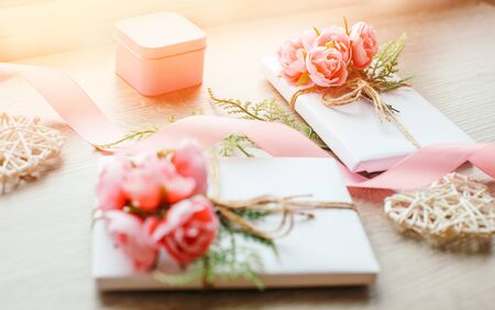 Gift boxes wrapped with simple white craft paper and bouquet of roses. Little pink giftbox and satin pink ribbon and wooden heart. Selective focusの写真素材