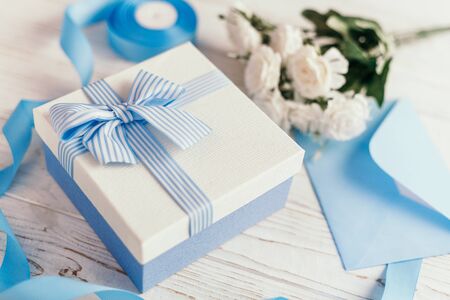 Gift box with blue ribbon and bow. Simple composition with present wrapped. Giftwrap, silk ribbon. Floral decor elements.の写真素材