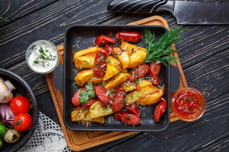 Poster for Restaurants. Potato baked with sausages along with white and red sauce. On a black wooden background. Flay lay. Top viewの写真素材