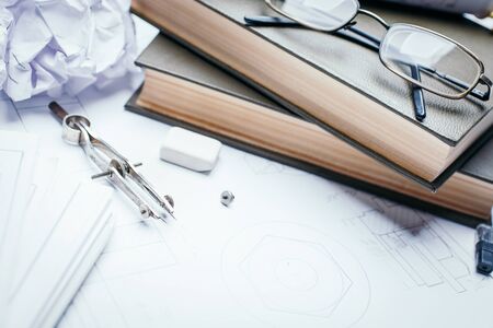 Books, glasses, pencil, compass and rolls of drawings on the details of industrial drawings. Engineering and technology. Technical drawing.の写真素材