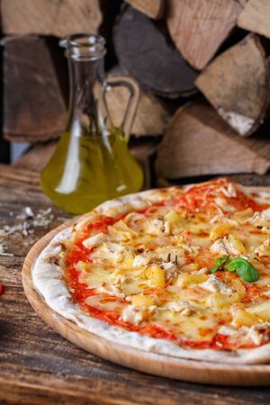 Pizza with chicken and pineapple on the background of firewood and olive oil. Creative layout. Pizza on a wooden backgroundの写真素材