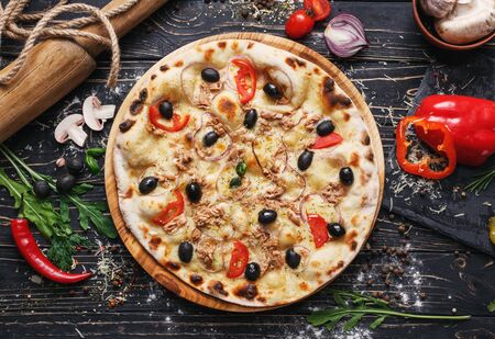 Exquisite pizza with fish, olives and onions. Poster for Restaurants or pizzerias. Pizza on a black wooden background among spicesの写真素材