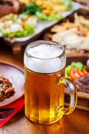 A glass of light beer on the background of a table with snacks. A glass of light beer with foam on a wooden table in the pubの写真素材