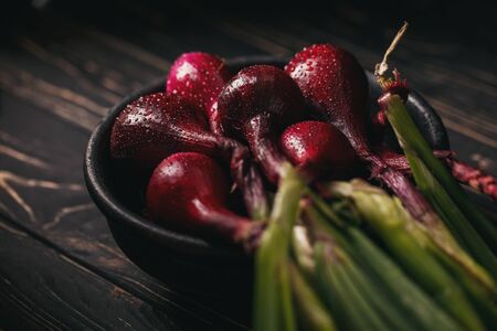 In a black clay plate onions with leaves. Wet onions. On a dark backgroundの写真素材