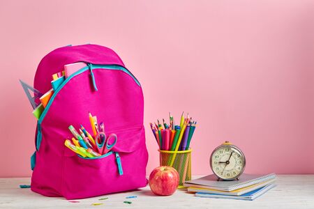 Pink briefcase next to pencils and a clock on a pink background. The briefcase is ready for returning to school. Background ready for your design. School and office supplies frameの写真素材