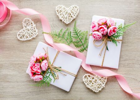 Eco style gift wrapping. Composition with gift boxes decorated with green branch, rose, wooden hearts and satin pink ribbon. Top view, flat layの写真素材