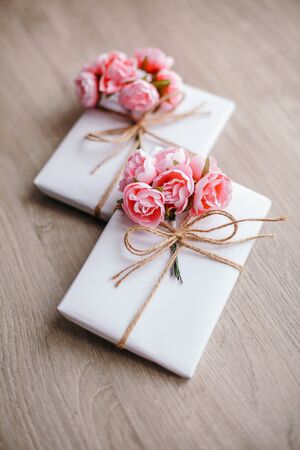 Couple of gift boxes wrapped with simple white craft paper and decorated with bouquet of roses and bunch of eucalyptus.の写真素材