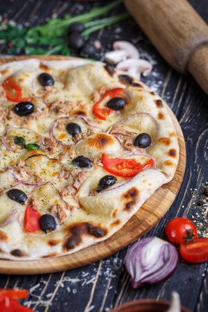 Pizza with fish, olives, onions and tomatoes near vegetables. Concept promotional flyer. Pizza on a black backgroundの写真素材