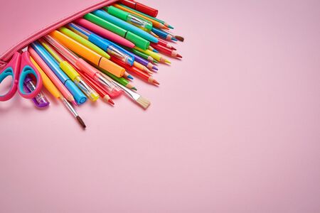 Bright stationery in the pencil case is lying on a pink background. Stationery with copyspace. School supplies on the left side of the background. Flat lay. copyspaceの写真素材