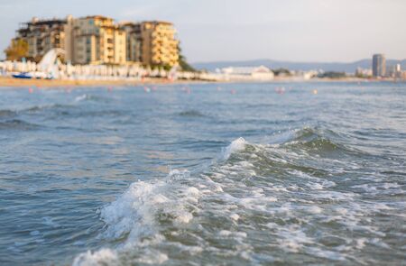 Sea waves on a warm summer day. Sunny beach. Tourist hotel on the backgroundの写真素材
