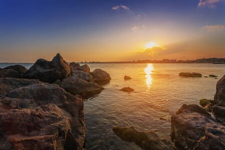 A magical sunset above the city by the sea. Rocks in the foregroundの写真素材