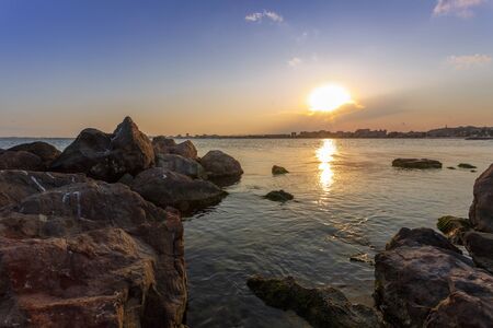 A magical sunset above the city by the sea. Rocks in the foregroundの写真素材