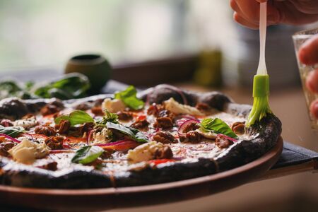 Delicious background. The cook lubricates the pizza with ham and basil with olive oil. Close upの写真素材