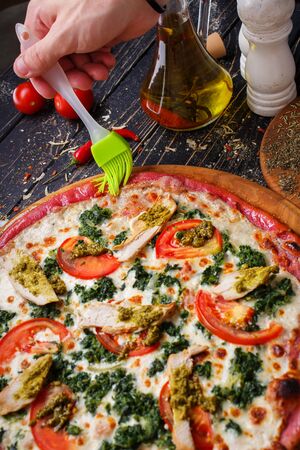 Pizza with chicken, tomatoes, greens and cheese. The cook packs the olive oil. Top view.の写真素材