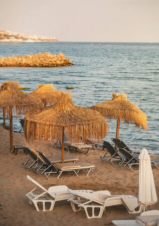 Empty beach loungers on the sandy beach near the sea. A quiet place to relax under straw umbrellas.の写真素材