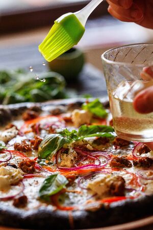 Closeup hand of chef baker making pizza at kitchen. The cook lubricates the traditional Italian pizza with olive oilの写真素材