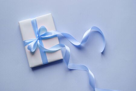 Decorative white gift box with blue bow and long beautiful ribbon on a blue background. Top viewの写真素材