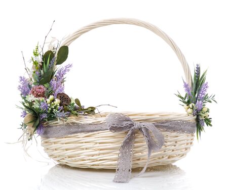 Natural wicker basket with flowers and ribbons. Beautiful floral decor on the side on the basket handle. Isolated on a white background.の写真素材